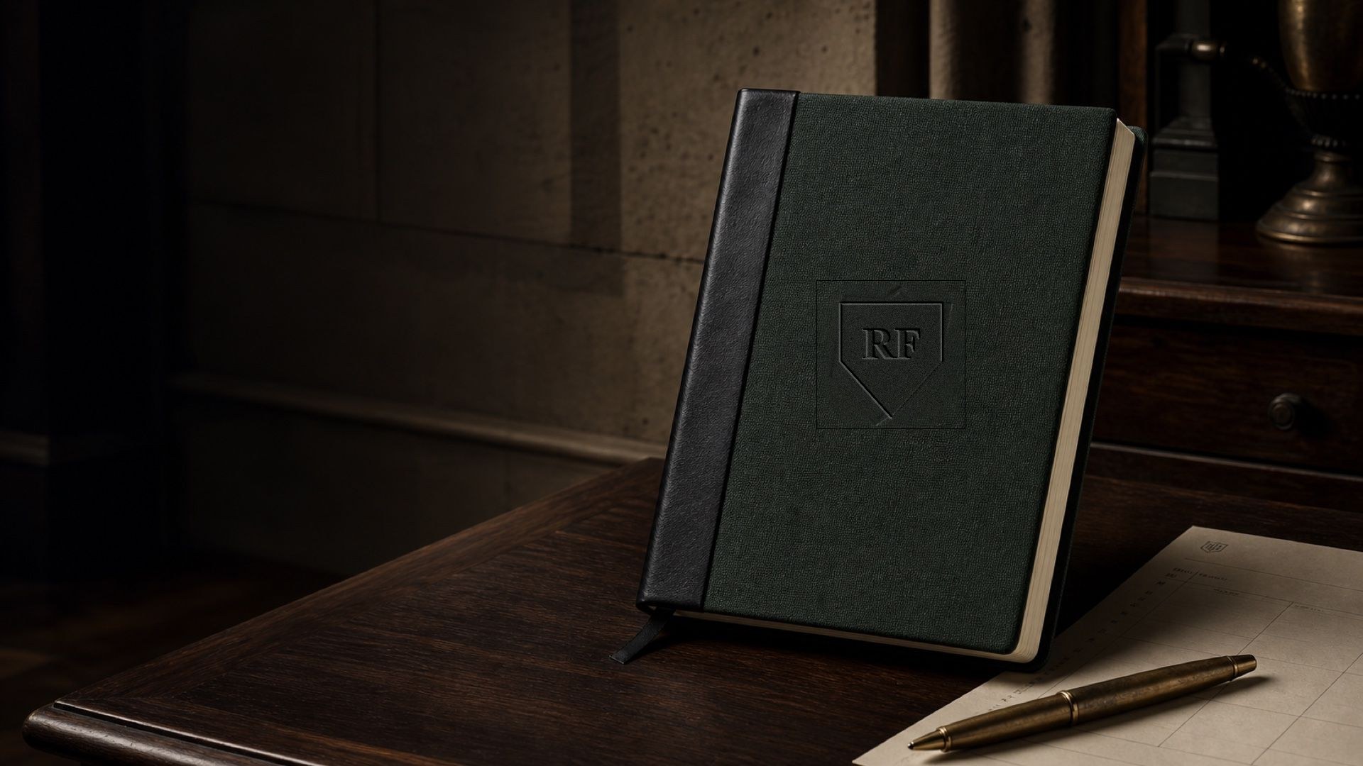 Forest-green clothbound operating journal with black leather spine on a dark walnut desk